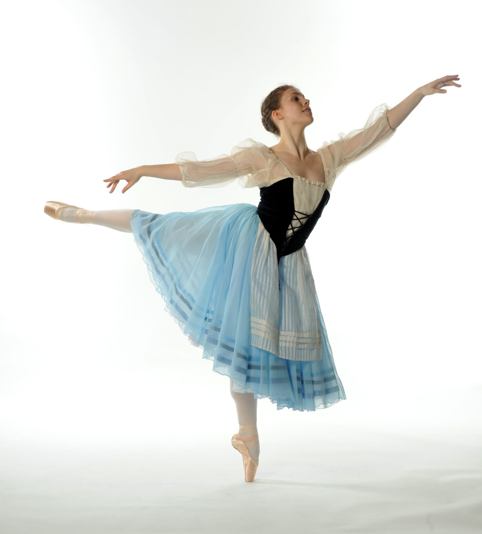 Natasha in first arabesque, wearing a Giselle costume with blue skirt, black bodice, and gauzy white sleeves