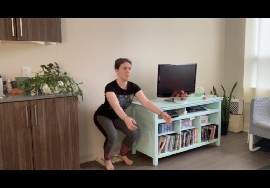 Natasha facing away from the wall and doing a squat with her heels elevated on a book.